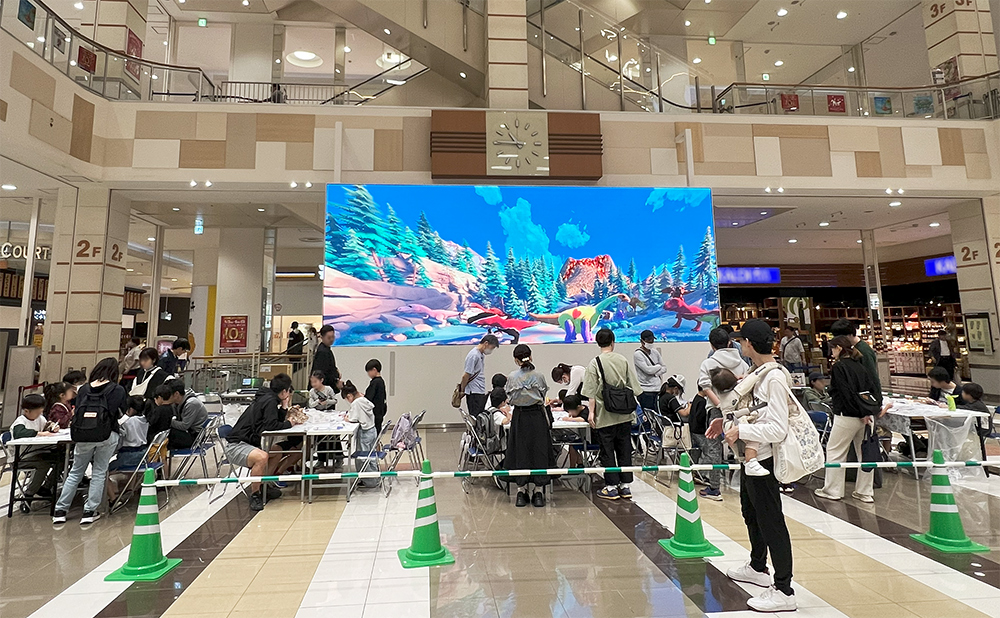 会場ホールの大画面モニターに映る「おえかきパラダイス恐竜3D」と親子連れの参加者たち